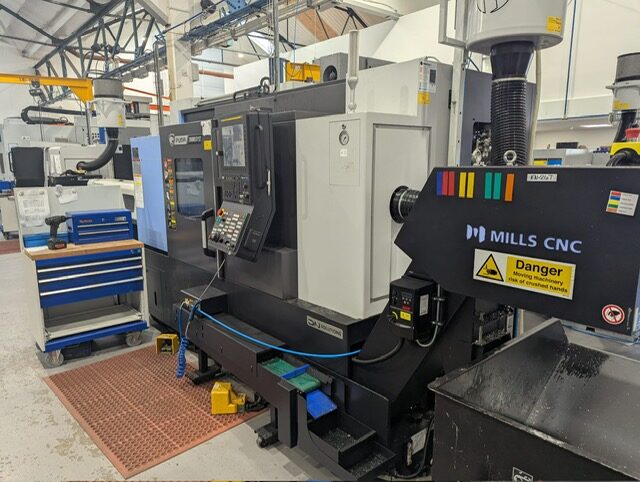 CNC milling machine in factory workshop with control panel and safety signage