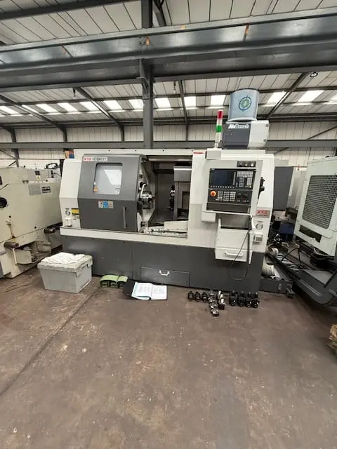 CNC lathe machine with control panel inside an industrial workshop with tooling on the floor